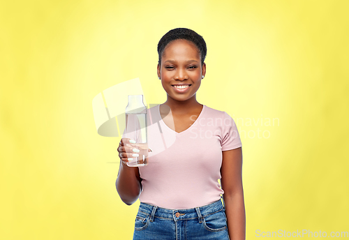 Image of happy african woman drinks water from glass bottle