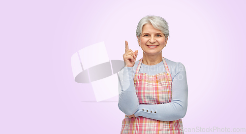 Image of smiling senior woman in apron pointing finger up