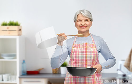 Image of smiling senior woman with frying pan at kitchen