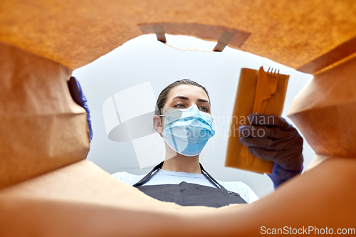 Image of saleswoman in gloves and mask packing food in bag