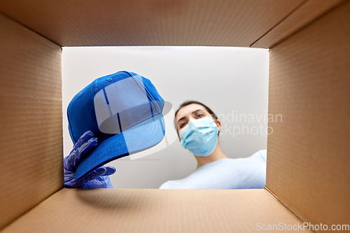 Image of woman in mask opening parcel box with clothes