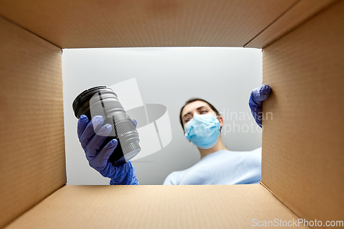 Image of woman in mask packing camera into parcel box