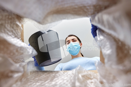 Image of woman in mask opening parcel box with flower pot
