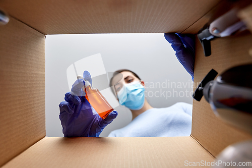 Image of woman in mask unpacking parcel box with cosmetics