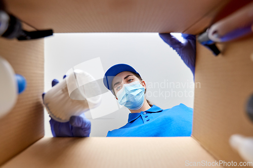 Image of woman in mask unpacking parcel box with cosmetics