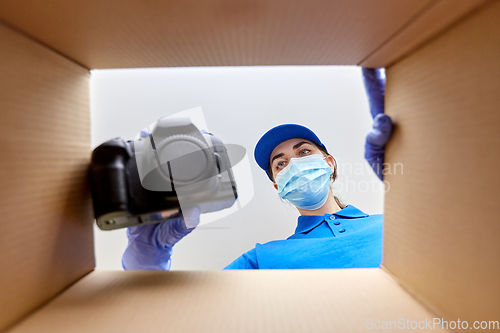 Image of woman in mask packing camera into parcel box