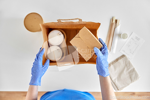 Image of delivery woman in gloves packing food and drinks