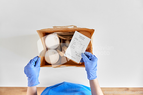 Image of delivery woman in gloves packing food and drinks