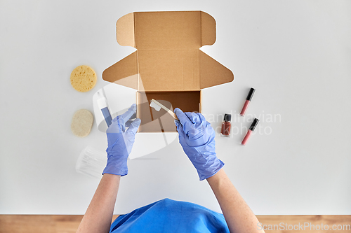 Image of hands in gloves packing parcel box with cosmetics