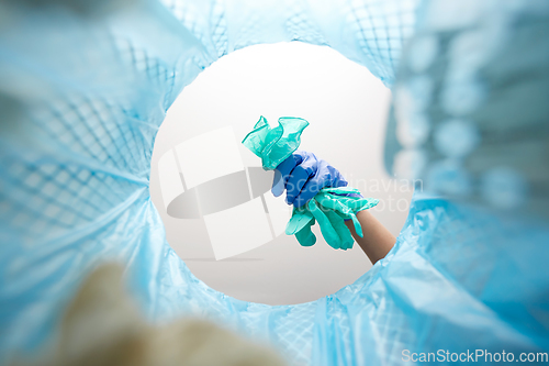 Image of hand throwing used medical gloves into trash can