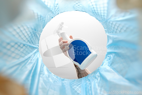 Image of hand throwing bottle of detergent into trash can