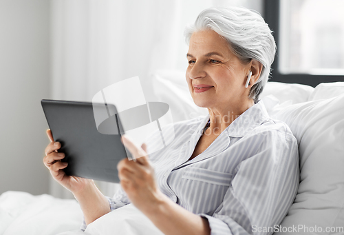 Image of senior woman with tablet pc and earphones in bed