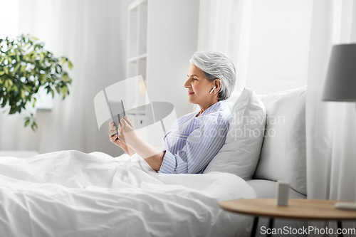 Image of senior woman with tablet pc and earphones in bed