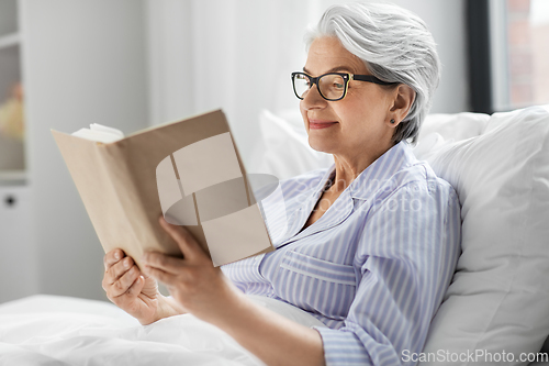 Image of old woman in glasses reading book in bed at home