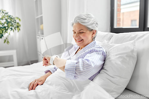 Image of happy senior woman sitting in bed at home bedroom