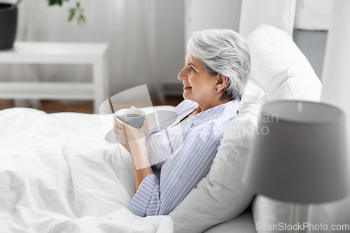 Image of old woman with cup of coffee in bed at home