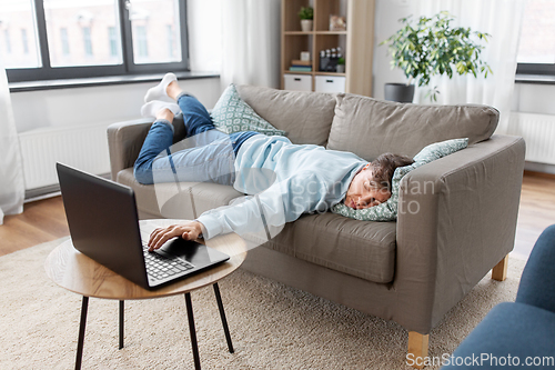 Image of bored man with laptop lying on sofa at home