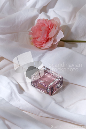 Image of bottle of perfume and flower on white sheet