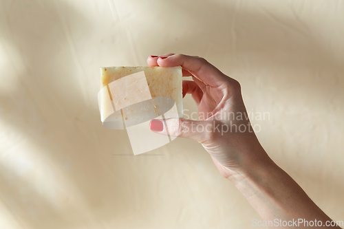 Image of hand holding bar of craft soap on beige background