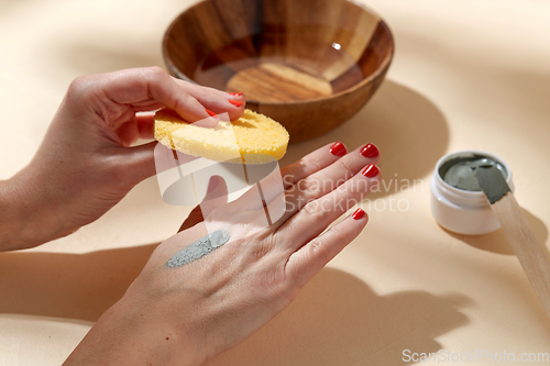 Image of hands applying blue cosmetic clay mask to skin