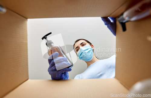 Image of woman in mask unpacking parcel box with cosmetics