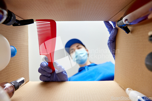 Image of woman in mask packing parcel box with cosmetics