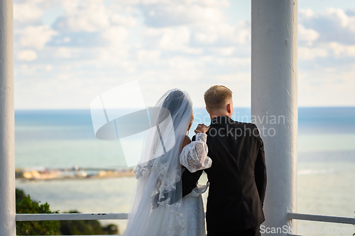 Image of Newlyweds in a beautiful gazebo look into the distance at the sea