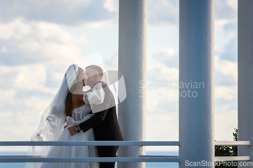 Image of The newlyweds happily kiss in a beautiful picturesque gazebo against the sky