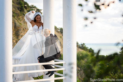 Image of The newlyweds are walking in a beautiful picturesque gazebo, the girl is holding a veil with her hand, the guy is sitting on the railing