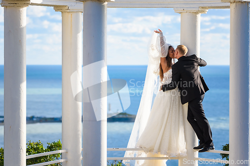 Image of Newlyweds kiss in a beautiful gazebo standing on a metal railing