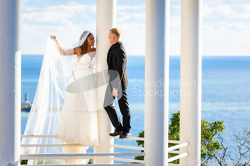 Image of Newlyweds in a beautiful gazebo stand on a metal railing against the backdrop of the sea