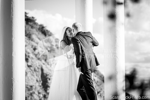 Image of Happy newlyweds kiss in a beautiful gazebo with columns against the background of foliage and sky, black and white version