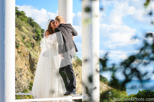 Image of Happy newlyweds kiss in a beautiful gazebo with columns against the backdrop of foliage and sky