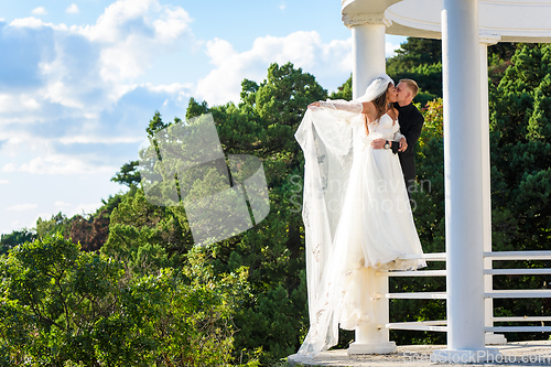 Image of The newlyweds happily embrace in a beautiful gazebo with columns against the backdrop of foliage and sky