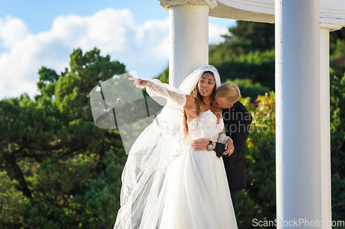 Image of The groom kisses the neck of the bride, the bride shows her hand into the distance