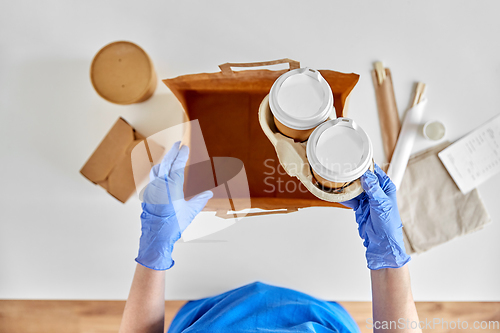 Image of delivery woman in gloves packing food and drinks