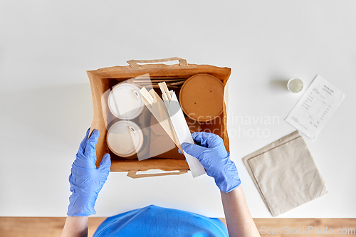 Image of delivery woman in gloves packing food and drinks