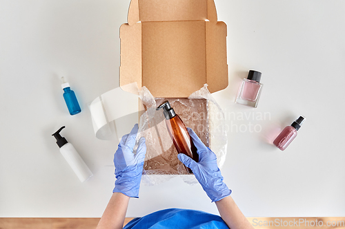 Image of hands in gloves packing parcel box with cosmetics