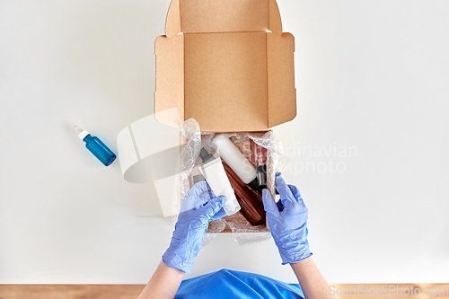Image of hands in gloves packing parcel box with cosmetics