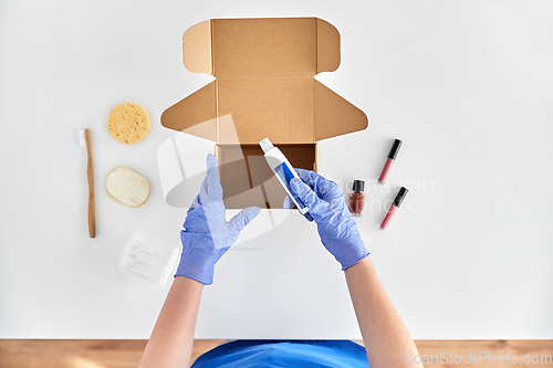 Image of hands in gloves packing parcel box with cosmetics