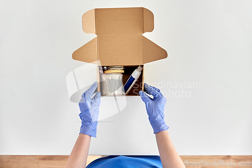 Image of hands in gloves packing parcel box with cosmetics