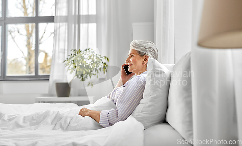 Image of senior woman calling on smartphone in bed at home