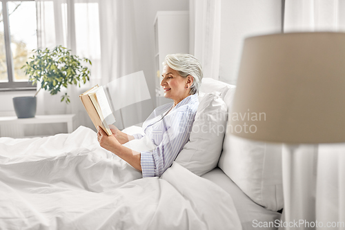 Image of senior woman reading book in bed at home bedroom