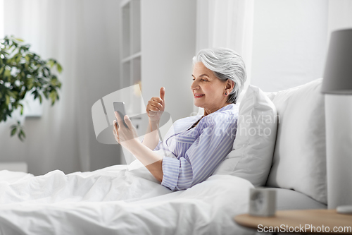 Image of senior woman with phone having video call in bed