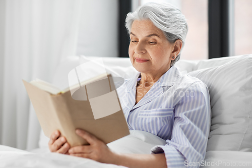 Image of senior woman reading book in bed at home bedroom