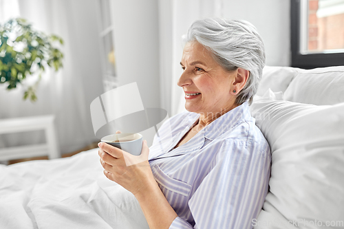 Image of old woman with cup of coffee in bed at home