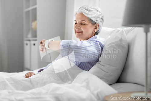 Image of happy senior woman sitting in bed at home bedroom