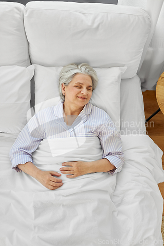 Image of happy senior woman sleeping in bed at home bedroom
