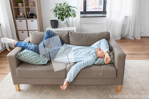 Image of bored or lazy young man lying on sofa at home