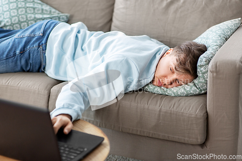 Image of bored man with laptop lying on sofa at home